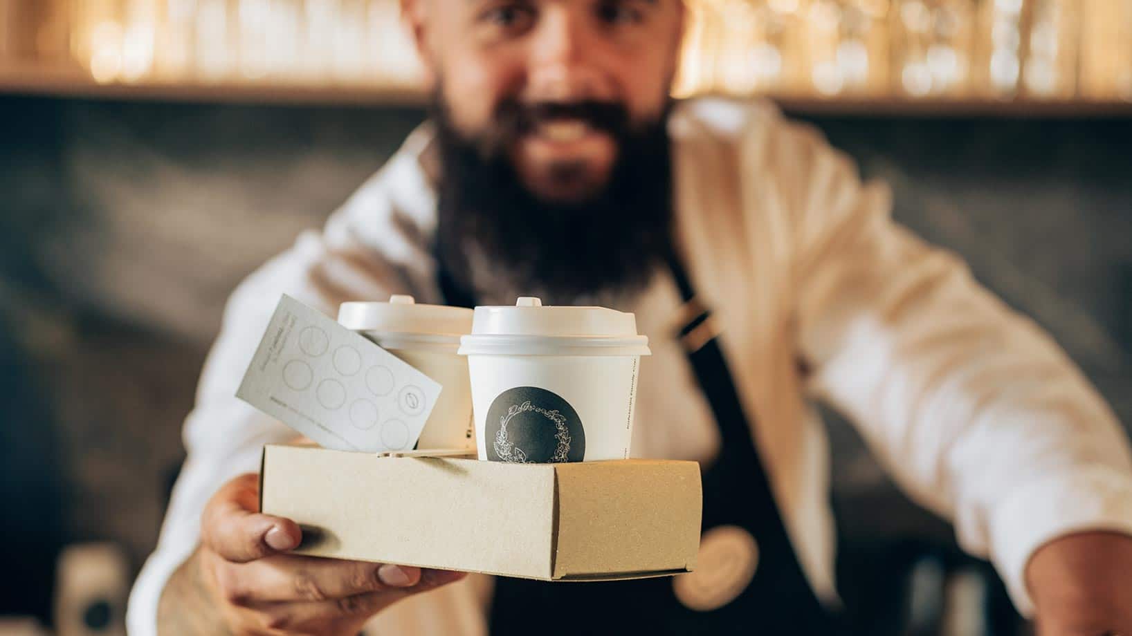 Ein Mann mit zwei Bechern Kaffee sowie einer Punktekarte als Beispiel für Kundenbindungsprogramme.