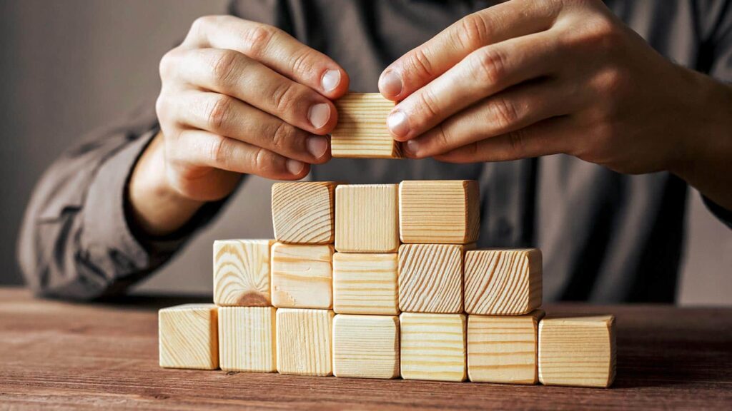 Auf dem Bild ist ein Mann zu sehen, der aus Holzklötzen eine Pyramide baut.